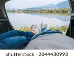 Two pairs of jeans dressed legs in white sneakers. Couple relaxing in camper trunk and enjoying mountain autumnal lake views. Cozy early autumn couple auto traveling concept image.  