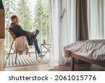 Small photo of Alone man sitting in chair on country house balcony and enjoying forest view, tea cup, fresh air and bestseller novel thick book. Cozy bedroom interior back view. Reading or education concept image