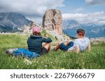 Mother and son backpackers have a tea brake on a green mountain hill with the picturesque Dolomite Alps Cinque Torri formation, Nothern Italy. Family values, active people and mountains concept. 
