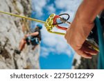Small photo of Belay device close-up shot with a boy on the cliff climbing wall. He hanging on a rope in a climbing harness and his partner belaying him on the ground. Active people and sports concept image