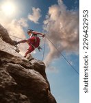 Small photo of Muscular climber man in protective helmet abseiling from cliff rock wall using rope Belay device and climbing harness on evening sunset sky background. Active extreme sports time spending concept.