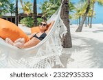 Small photo of Smiling middle-aged woman relaxing lying in wicker hammock in palm trees grove on white sandy beach on Mauritius coast and enjoying . Exotic countries vacation and mental health concept image