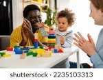 Small photo of Mother and father supporting their cute little daughter in playing with colorful didactic wooden toys at home