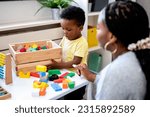 Small photo of A cute little African child plays with colorful didactic educational toys. His proud mother supports him. Kindergarten teacher with child.