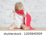 Indoor portrait of a cute blond baby wearing a red wool shawl, playing a peekaboo game or don't want to dress up concept