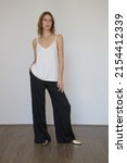 Small photo of Female model wearing white camisole cotton top and black trousers. Classic and simple summer fashion. Studio shot.