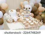 Small photo of Creative gender neutral baby shower or birthday decoration in the garden. Bohemian style outdoor event set up with balloons. White cream peach caramel balloon arch kit. Sweet table for a party