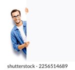 Small photo of Portrait image of happy smiling casual man in eye glasses hold, peep out, stand behind mockup blank signboard, billboard, isolated over white background. White empty ad sign board banner. IT Expert