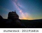 Figure stargazing atop rocks beneath the Milky Way, Dartmoor National Park, UK