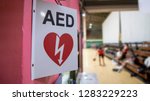 Small photo of An automated external defibrillator symbol in front of the gymnasium. The AED using in emergency situation such as acute cardiac arrest. The basketball players was playing in blurred background.