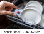 Close up of woman hand filling dishwasher tablet into open automatic stainless built-in dishwasher machine with dirty white dish inside in modern home kitchen.Household, housekeeping domestic life.