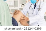 Small photo of The orthopedic doctor or surgeon in white gown examined the patient with knee pain problem.White clean table or bed with blur background.Knee ligament or meniscus sport injury.Orthopaedic unit.