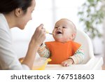 Mother feeding her baby son with spoon. Mother giving healthy food to her adorable child at home