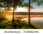 Summer camping on the lake. Empty hammock  between two trees with the view of a foggy mountain lake in sunrise light. Outdoors and adventure concept.