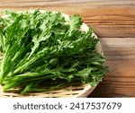 Small photo of Garland chrysanthemum in a bamboo colander placed against a wooden background. Garland chrysanthemum is an Asian vegetable.