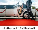 Driver helping VIP woman or star out of limo on red carpet to a reception