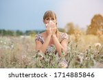 Small photo of A woman sits in a hay meadow and snorts in a handkerchief