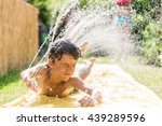 Boy cooling down with garden hose, family in the background on a hot summer day