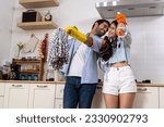 Small photo of Young happy couple having fun while doing cleaning kitchen, They hold a mops and rags with spray bottle in hands and happily teasing each other, Happy family concept