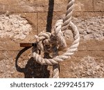 Small photo of Knot on a thick white rope tied to an oarlock against the background of a stone brick wall front view