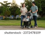 happy parent (father and mother) talking and pushing infant baby stroller and walking in the park