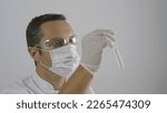 Small photo of scientist with eyeless and mask looks at the test tube