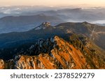 Beautiful sunset over mountain range with rocky terrain and greenery.Sun is setting behind mountains, casting warm glow over landscape.