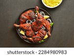 Small photo of Indian style tandoori chicken on plate over dark stone background. Chicken legs marinated in yogurt and spices. Top view, flat lay