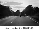 Antique car driving down highway in black and white.