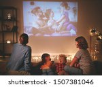 family mother father and children watching projector, TV, movies with popcorn in the evening   at home 
