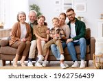 Big happy family. Portrait of grandparents, mother, father and two their cute kids, sister and brother, sitting together on coach at home and smiling at camera. Mortgage loan and real estate concept