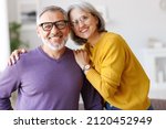 Small photo of Portrait of happy beautiful senior caucasian family couple in love smiling at camera, retired man and woman hugging embracing while relaxing on sofa in living room at home, enjoying life on retirement