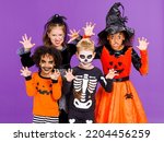 Happy Halloween! Cheerful kids in carnival costumes and makeup make a terrible gesture on bright colored purple background