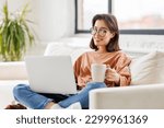 young beautiful woman drinking delicious hot coffee while surfing internet at laptop on sofa at home