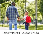Small photo of On way to school. Ethnic son schoolboy with backpack holding hand of father, boy looking at dad with smile while going to first grade on sunny autumn day through park