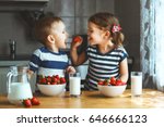 Happy children girl and boy brother and sister eating strawberries with milk