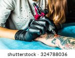 Master tattoo draws the orange paint on the clients tattoo. Tattoo artist holding a pink tattoo machine in black sterile gloves and working on the professional blue mat. 