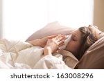 Young sick woman blowing her nose while in bed