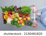 Small photo of Woman pushing a shopping cart full of vegetables and fruits, healthy food and grocery shopping concept, top view