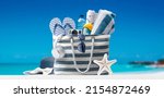Small photo of Stylish beach bag with accessories and tropical beach in the background, summer vacations concept