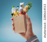 Small photo of Customer holding a miniature paper bag with fresh groceries falling inside, grocery shopping concept