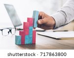 Businessman working at office desk, he is building a growing financial graph using wooden toy blocks: successful business concept