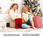 Two beautiful blond women. Models posing near decorated Christmas tree at New Year eve. Having fun, ready for celebration. Bright holiday of best friends dressed in warm winter sweaters