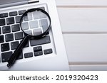 Magnifying glass laying on a laptop keyboard. Technology file search tool concept, data forensics, computer crime and device investigation, closeup