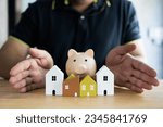 Small photo of Man showing many wood model house and piggy Bank. Savings for buying home. House trading concept. Housing, bank loans to buy a house, real estate investment, real estate business.