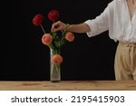girl holding a dahlia flower in a glass vase on a wooden table, dark background, mockup