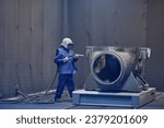 Small photo of worker processes workpiece with sandblasting tool in factory, selective focus