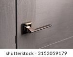 Close up of stylish new metal door knob on modern interior door. Shiny silver door handle on light gray door. Concept of interior details.