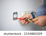 Man doing electrics. Close up of man installing electrical outlet in wall in room of house. Male electrician uses screwdriver to tighten bolts while attaching metal part of socket to wall.