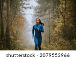 Small photo of Young woman in blue track suit running toward camera on the forest trail at autumn